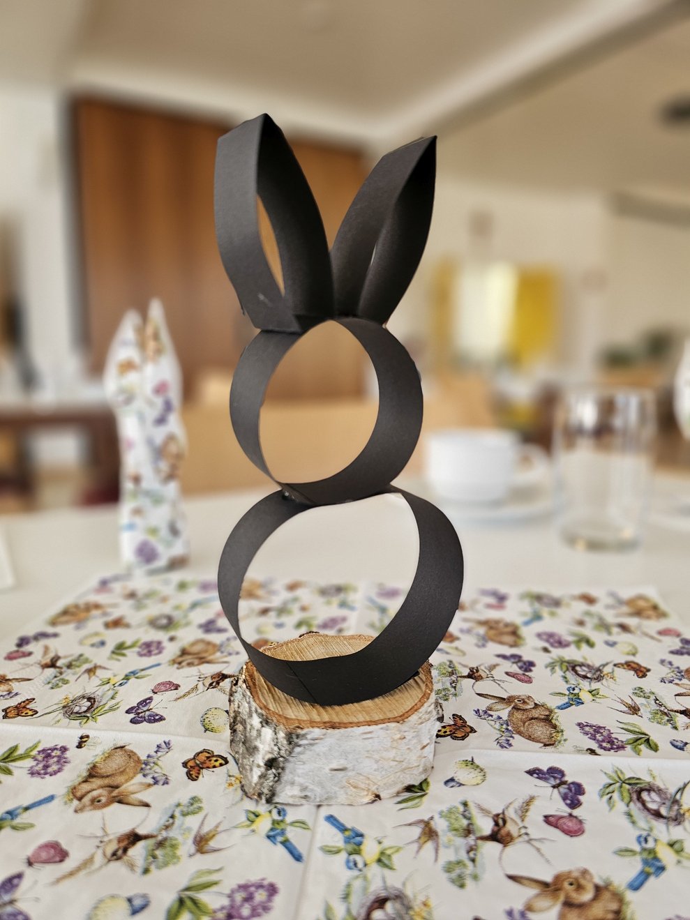 Unsere selbst gestaltete Tischdekoration. Ein Osterhase aus Papierstreifen auf einer Holzscheibe.